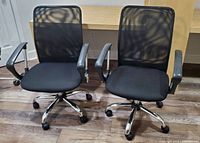 Front view of two matching black office chairs with mesh backs and padded seats, armrests, and five-star chrome bases with wheels.