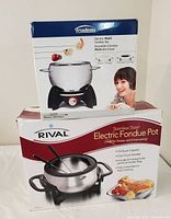 Photo of two boxed fondue sets stacked, Trudeau on top and Rival below.