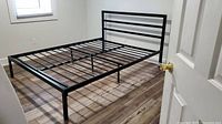 Black metal queen bed frame with attached headboard standing assembled in a room, showing width and height.