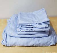 Light blue queen size folded sheet set including fitted and flat sheets, along with six pillowcases stacked on a surface.