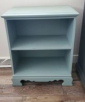 Front view of the blue/green painted bookcase showing two shelves and decorative base.