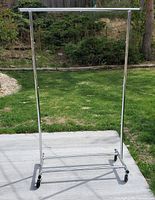 Full view of the chrome portable clothes rack standing on concrete with grass background. Shows overall rack including top bar and supporting structure.