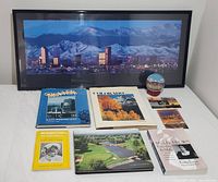 Framed Denver skyline poster, books, postcards, and decorative globes on table.