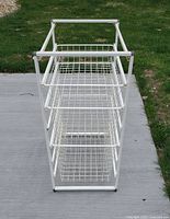 Front and slightly top view of the Elfa storage unit showing the 3 sliding wire baskets inside a white metal frame.