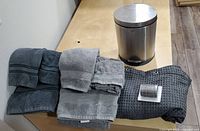 Photo showing all items: two sets of gray towels, dark waffle shower curtain, silver rings, and stainless steel step can.