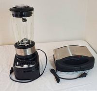 Hamilton Beach blender and Rival waffle maker shown side by side on a white surface, power cords visible.