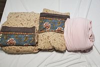 Three folded king size sheets on a white surface, two with floral and vine patterns and one solid pink fitted sheet.