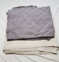 Photo showing two folded queen size blankets, one light grey with checkered pattern and one cream colored with loose weave texture.
