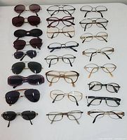 Various vintage eyeglasses and sunglasses laid flat on white surface, showing different styles and lens colors.