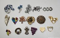 Full collection of 15 vintage pins and brooches, various shapes and colors, laid out flat on white background.