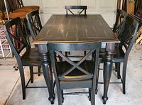 Front view of pub height rectangular wooden table with six chairs around it. Table has a black distressed finish with visible wear marks.