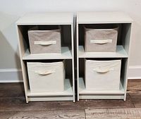 Front view of two Ikea Kallax cream storage cubes, each containing two fabric storage baskets (one beige, one cream). Cubes stand side by side on hardwood floor.