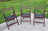 Three folding chairs placed on concrete sidewalk with grassy background, showing front view and overall condition.