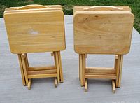 Two stacks of four blonde wood TV trays with stands, showing trays with varying degrees of surface wear and marks.
