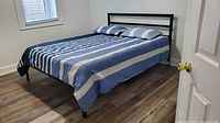 Bed made with reversible comforter and two matching pillow shams, striped blue and navy pattern.