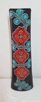 Full view of the tall cylindrical vase showing overall shape and decoration with repeating concho rosette patterns and turquoise leaf-like designs on black background.