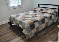 Full view of queen bed with tan and gray plaid patchwork bedspread and matching shams on pillows.