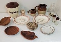 Full lot overview showing plastic cookie jar, monkey pod wood dishes, ceramic plates, glass salt and pepper shakers, apothecary jar, and pottery pieces.