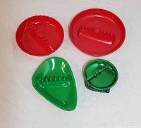 Four vintage ashtrays laid out flat, two red round melamine, one green atomic shaped, one green metal with plaid sides