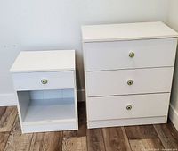 Photo of white nightstand and small dresser side by side showing overall condition, drawer fronts, and floral knob handles