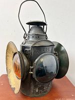 Full view of antique CPR railway signal lantern showing black metal body, metal handle, front dark blue glass prism lens, and orange side lens with reflector dish showing wear and chips.