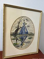 Frontal image of the framed watercolour painting showing the lady in blue by the lily pond with reflection and surrounding tree branches.