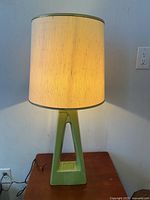 Front view of the mid-century modern table lamp with avocado green ceramic base and off-white fabric shade illuminated.