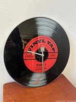 Full front view of the 17-inch diameter wall clock made to resemble a vinyl LP record with visible clock hands and red center label.