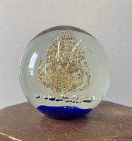 Front view of the clear spherical paperweight with internal gold jellyfish and blue base on a wooden surface.