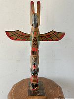 Front view of carved wooden First Nations totem pole with painted wings and animal faces