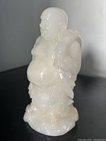 White jade carved Buddha sculpture, front-left angle showing detailed facial features and clothing.