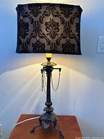 Full view of lamp showing bronzed metal base with tripodal claw feet and rectangular black damask patterned fabric shade.