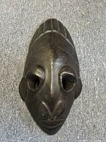 Front top-down view of leather-covered wood carved African tribal mask on a carpeted surface.