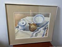 Framed watercolor painting titled "Orange & Blue" showing a sugar bowl, onion, and bowl on cloth.