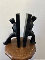 Front side view of pair of black modernist cubist style male figure bookends placed back-to-back on wood table.