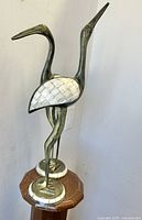 Pair of vintage standing crane bird sculptures made of metal with mother of pearl inlay on wings and base, displayed on a wooden surface.
