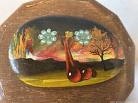 Surrealist oil painting on front of oval rock showing abstract red shapes, flowers, tree and fiery background
