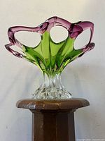 Front view of raspberry and green Murano glass bowl on pedestal with open cutouts and scalloped edges