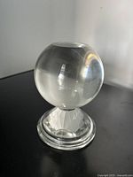 Side view of a solid clear glass witches ball on a multifaceted prismatic base, showcasing transparency and light refraction.