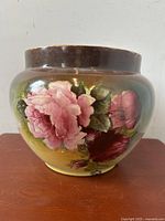 Front view of porcelain planter showing vibrant pink cabbage rose flowers and soft gradient background transitioning from yellowish green to brown near the rim.