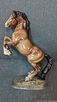 Glossy porcelain rearing horse figurine with brown coloring and black mane and tail, mounted on a grey mottled base, shown from a side angle.