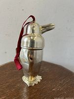Chrome plated miniature penguin-shaped cocktail shaker with red hanging loop on a wooden surface