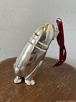 Front and side view of a chrome plated mini cocktail shaker shaped as a standing polar bear with a red ribbon attached to the head ring.