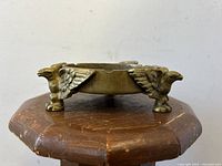 Side profile photo showing three-dimensional eagle feet supporting the round ashtray, highlighting the natural patina and metal detailing.