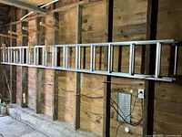 Wide view of aluminum extendable ladder mounted horizontally inside wooden shed walls.