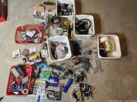 Overview photo showing multiple baskets and containers filled with assorted hardware, tapes, tools, and accessories laid out on a concrete floor.
