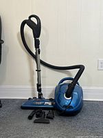 Blue Bissell vacuum with black hose and metal wand standing on carpet with attachments laid out
