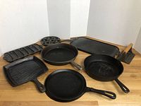 Overview of all seven cast iron pieces on wooden countertop against white backdrop.