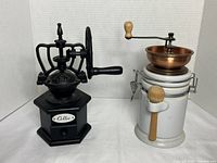 Black cast iron vintage coffee grinder with hexagonal base and drawer labeled 'Coffee', viewed from front and top angle showing metal crank handle with wooden knob and intricate wheel design