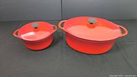 Both red enameled cast iron Dutch ovens side by side, oval and round shapes shown with lids on